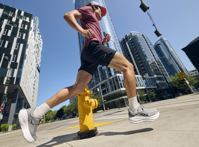 person running on sidewalk in a downtown area, wearing Hoka shoes.